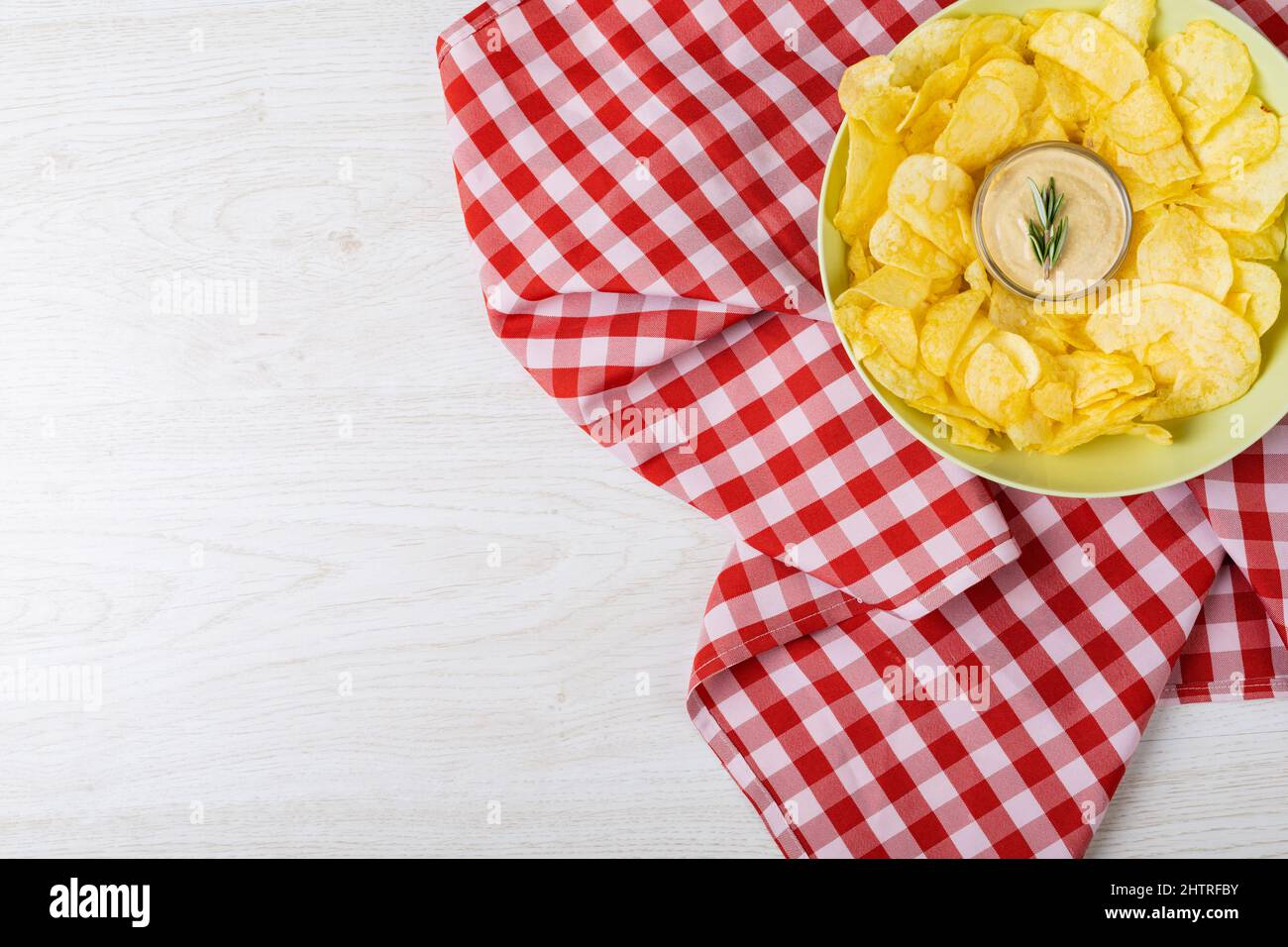 Blick von oben auf die Sauce inmitten von Kartoffelchips, die auf einem Teller auf karierter Serviette am Tisch serviert werden Stockfoto