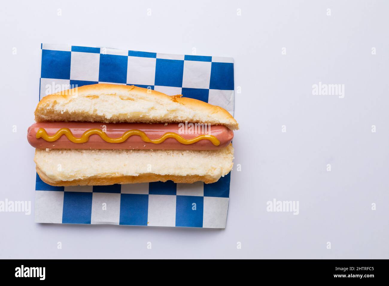 Direkt über Schuss Hot Dog mit Senfsauce auf kariertem Musterpapier auf weißem Hintergrund Stockfoto