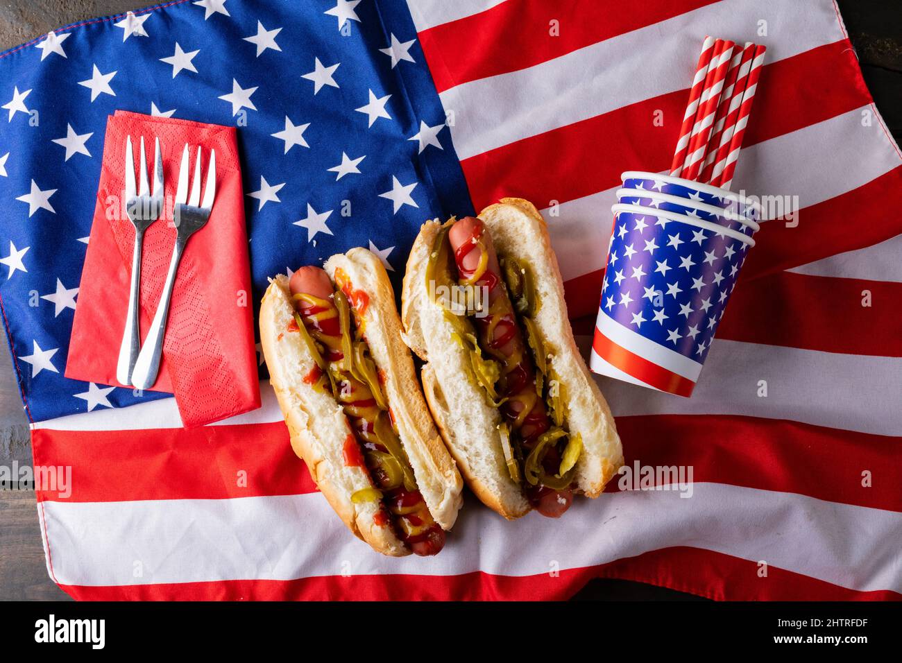 Hot Dogs mit Saucen und Jalapenos serviert auf amerikanischer Flagge mit Gabel, Stroh und Einwegbecher Stockfoto