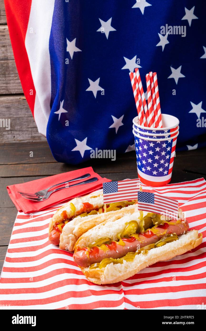 Hot Dogs serviert mit Jalapenos gegen amerikanische Flagge mit Gabel, Stroh und Einwegbecher am Tisch Stockfoto