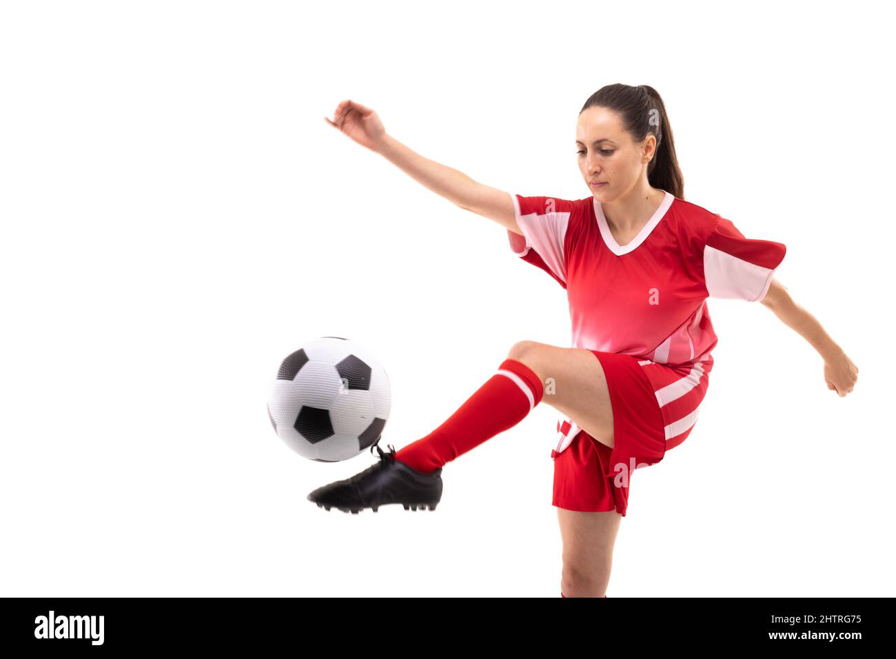 Kaukasische junge Fußballspielerin tritt beim Fußballspielen vor weißem Hintergrund den Ball Stockfoto