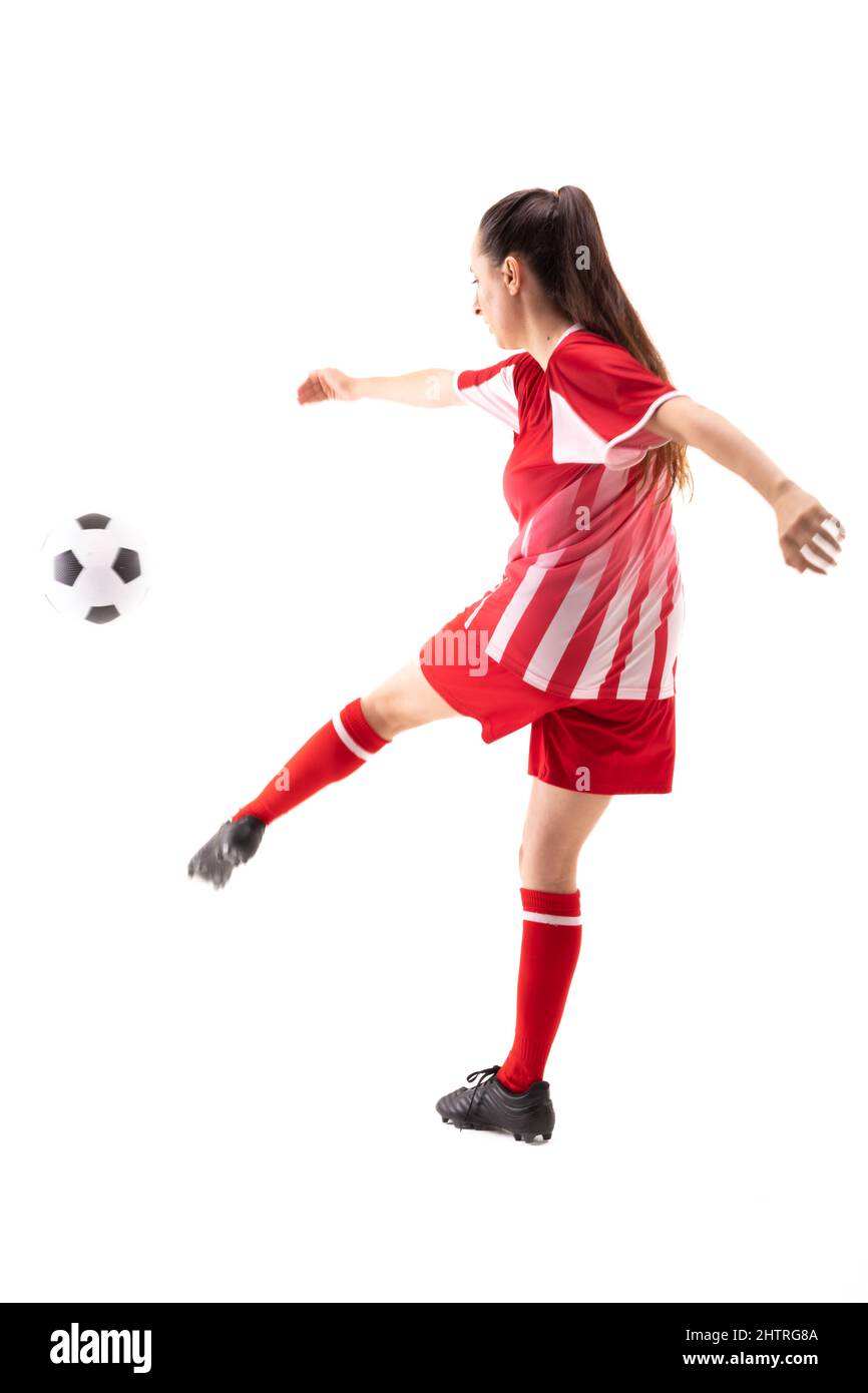 Die ganze Länge der kaukasischen jungen Fußballspielerin tritt den Fußball vor weißem Hintergrund Stockfoto