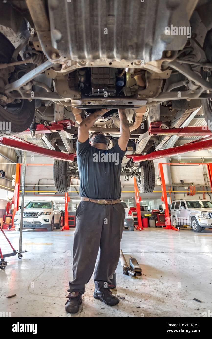 Lateinischer übergewichtiger Mechaniker, der unter einem schmutzigen Automotor arbeitet Stockfoto