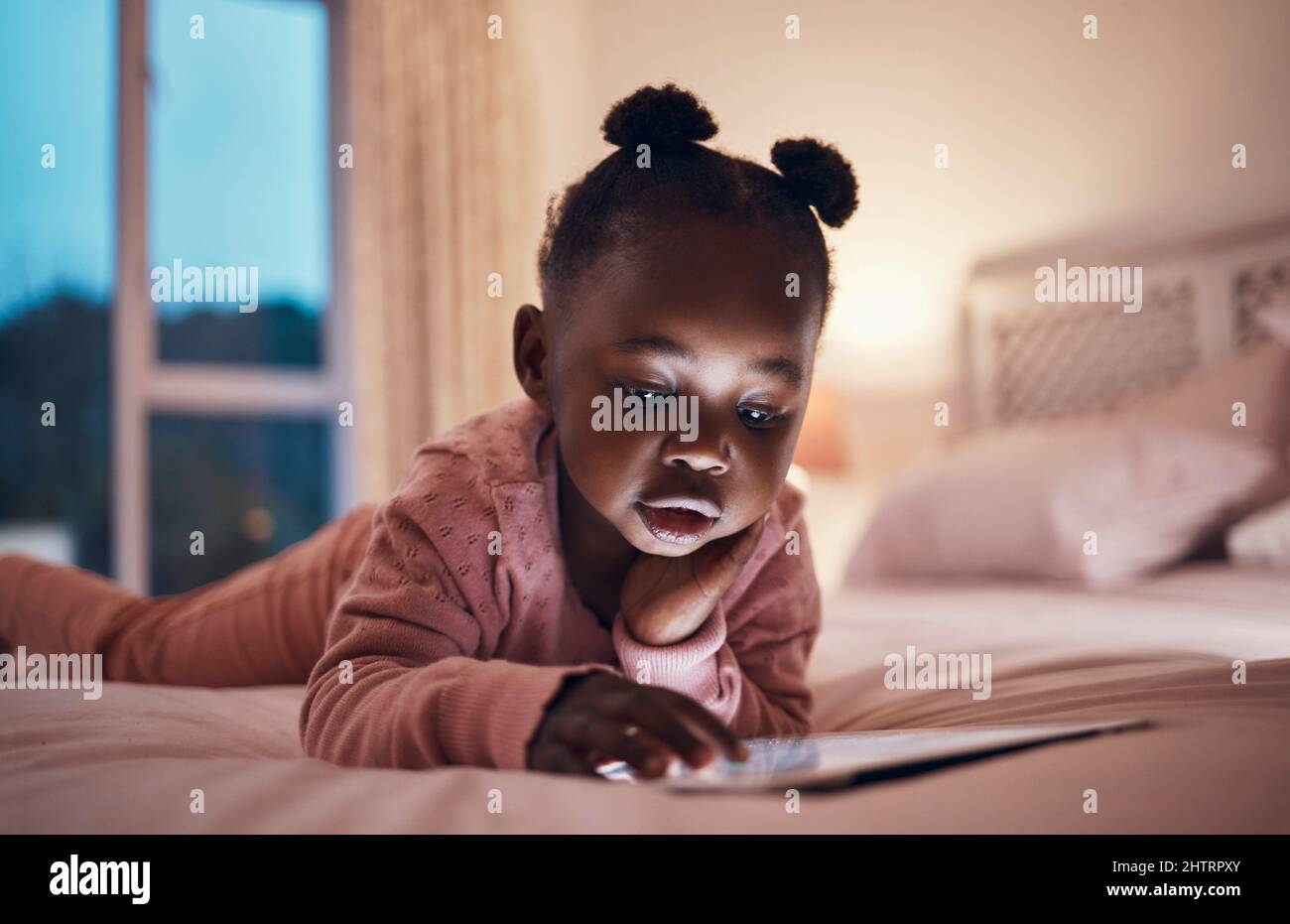 So viele Geschichten so wenig Zeit. Aufnahme eines kleinen Mädchens, das ihr digitales Tablet in ihrem Schlafzimmer benutzt. Stockfoto