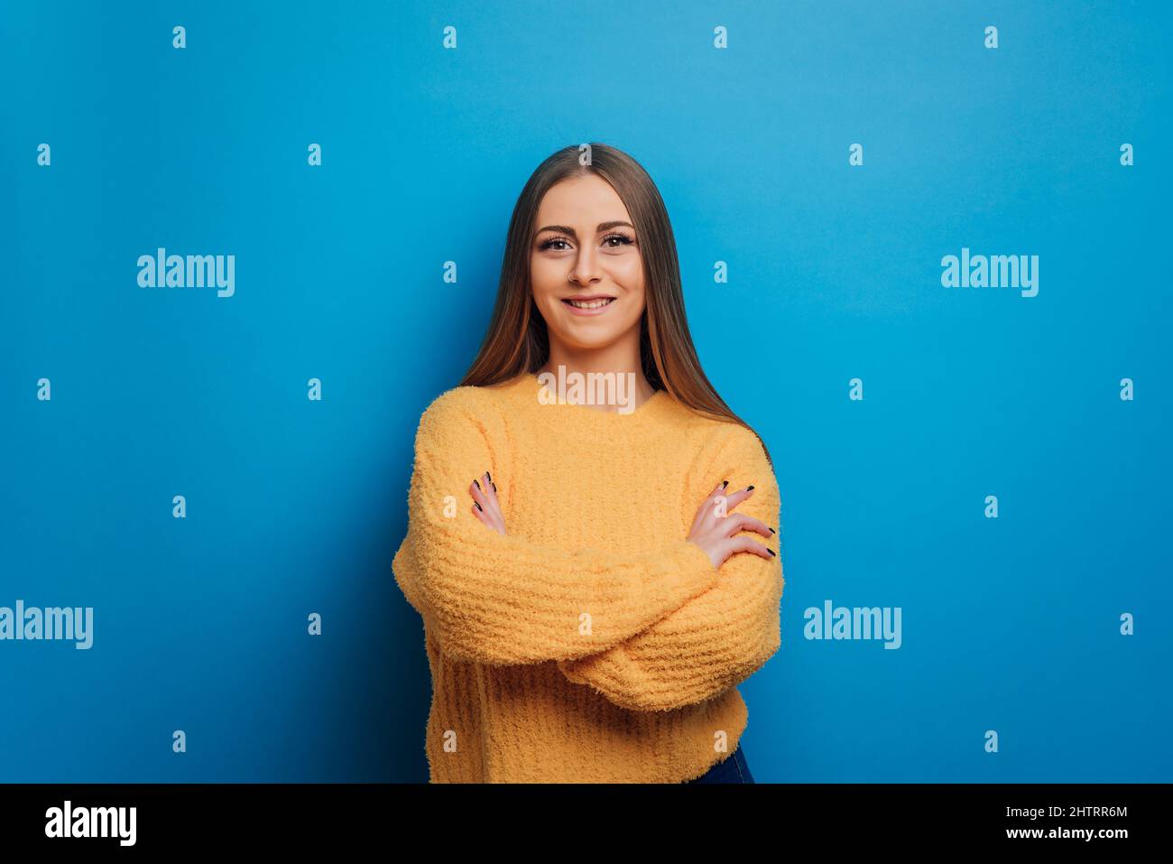 Frau, die die Kamera anschaut und lächelt, während sie mit gekreuzten Armen auf isoliertem Hintergrund posiert. Stockfoto