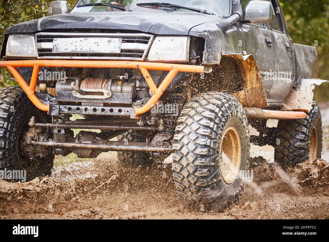 Geländefahrt auf schmutziger Offroad-Strecke auf einem schwarz-orangen LKW. Nahaufnahme des Rades, Aufhängung in einer Pfütze und Schlamm. Stockfoto