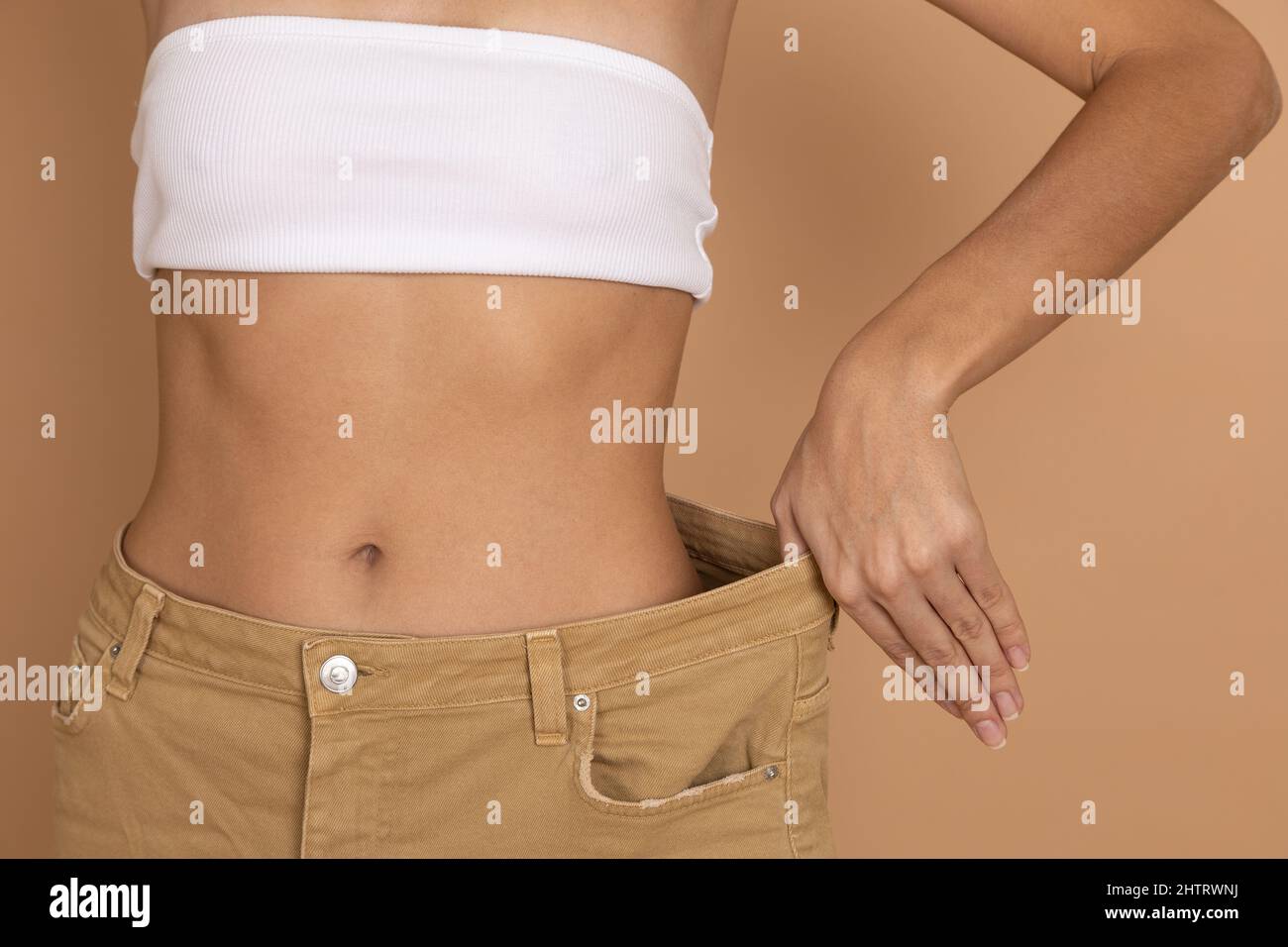 Nahaufnahme der Frau Taille in großen übergroßen Jeans mit Hand zeigt gute schlanke Form auf körperfarbenen Hintergrund. Gewichtsverlust durch die Aufrechterhaltung der Ernährung und Bewegung Stockfoto