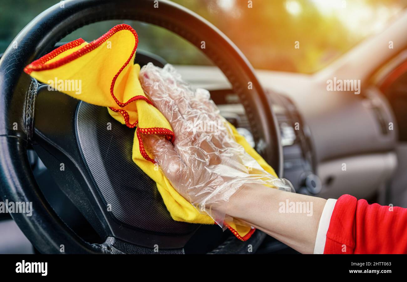 Junge Frau, die das Lenkrad im Auto mit einem gelben Wischtuch putzt, Details aus der Nähe zu ihrer Hand Stockfoto