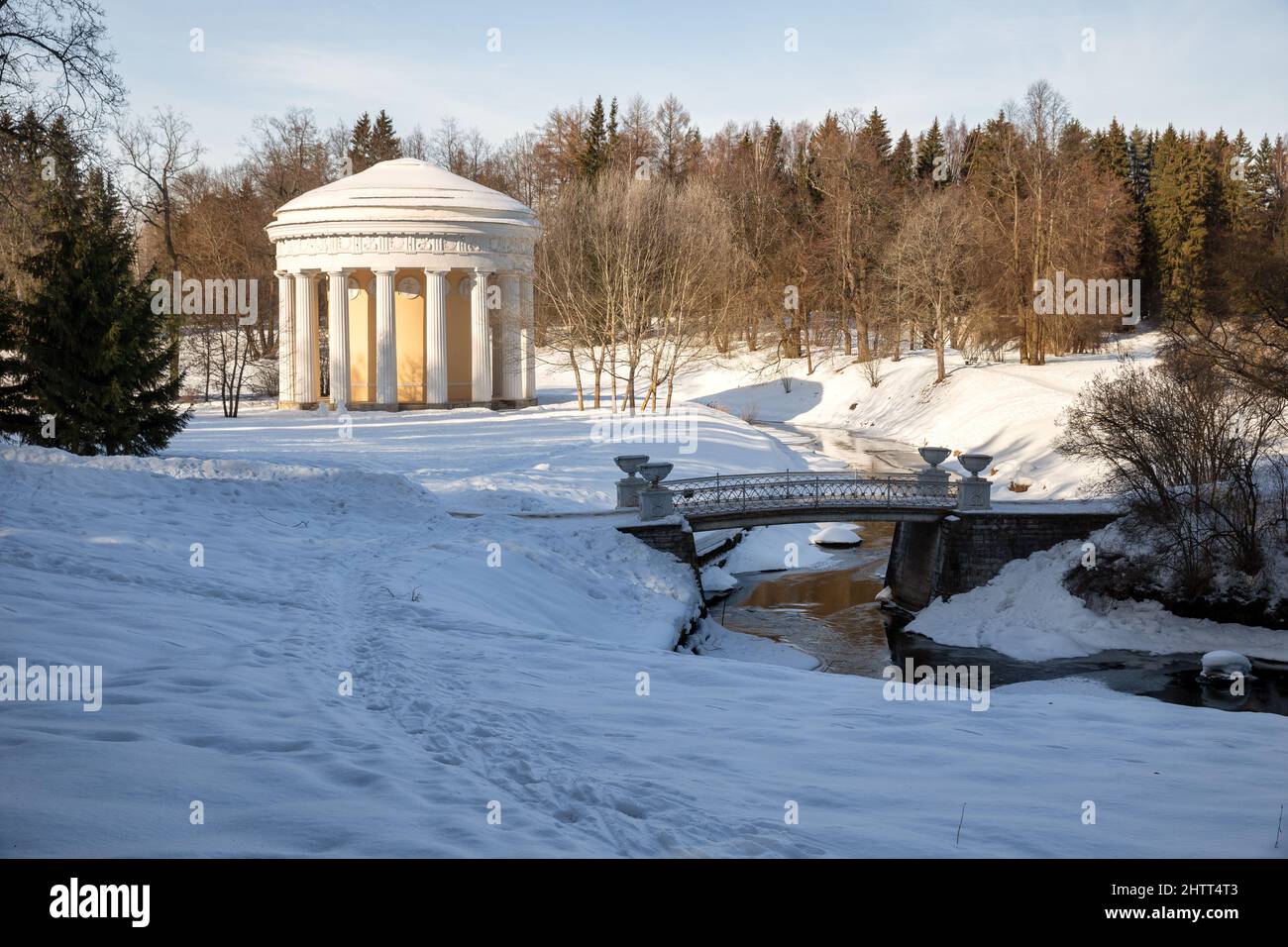 St. Petersburg, Russland - Februar 2022: Tempel der Freundschaft und eine gusseiserne Brücke über den Slawjanka-Fluss im Pawlowsker Park. Winterlandschaft Stockfoto