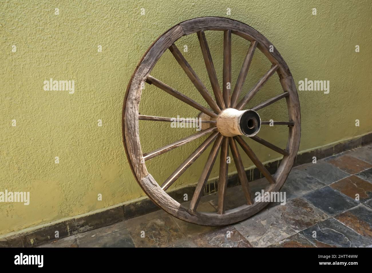 Veraltetes Vintage-Holzrad auf verblichenem gelben Wandhintergrund Stockfoto