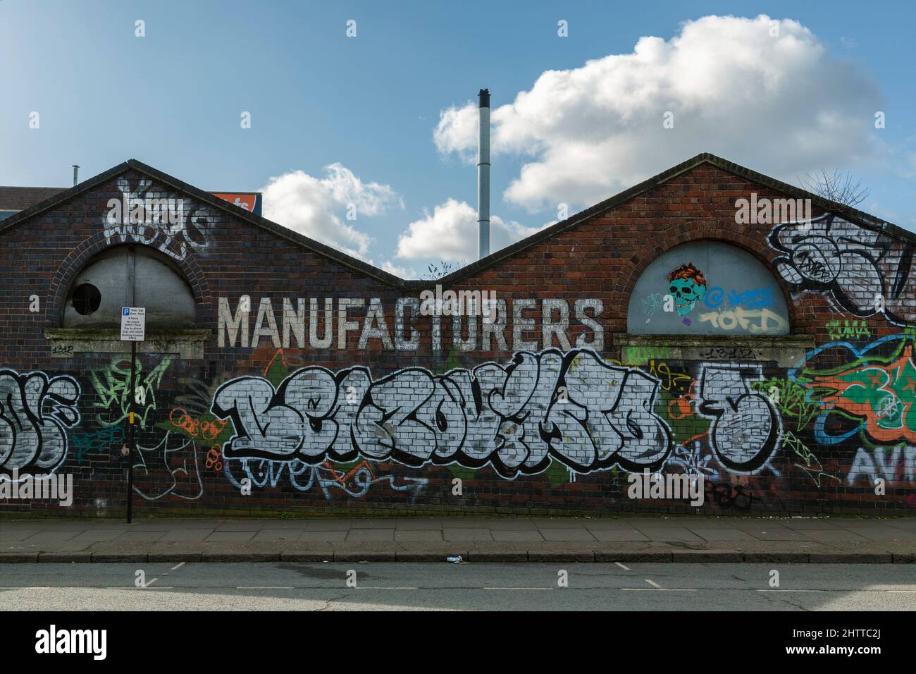 Eine mit Graffiti bedeckte Wand in einem alten Industrieviertel von Birmingham, Großbritannien, wird dem blauen Himmel und den Wolken darüber gegenübergestellt. Stockfoto