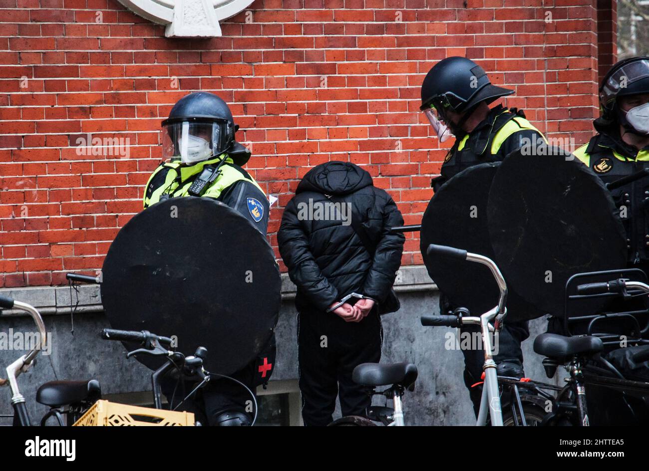 03-20-2021 Niederländische Bereitschaftspolizei in Amsterdam, Niederlande, mit einem jungen Mann in Handschellen, während eines Protestes gegen Zwangsmaßnahmen verhaftet Stockfoto