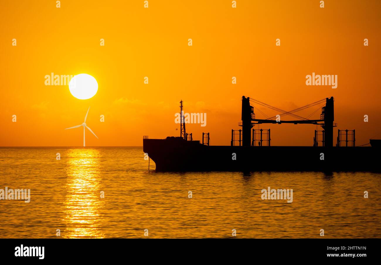 Oli-Tanker bei Sonnenaufgang mit Windturbine unter aufgehender Sonne. Konzept: Erneuerbare Energien, globale Erwärmung, fossile Brennstoffe, globale Erwärmung, Klimawandel, Netto, Null Stockfoto