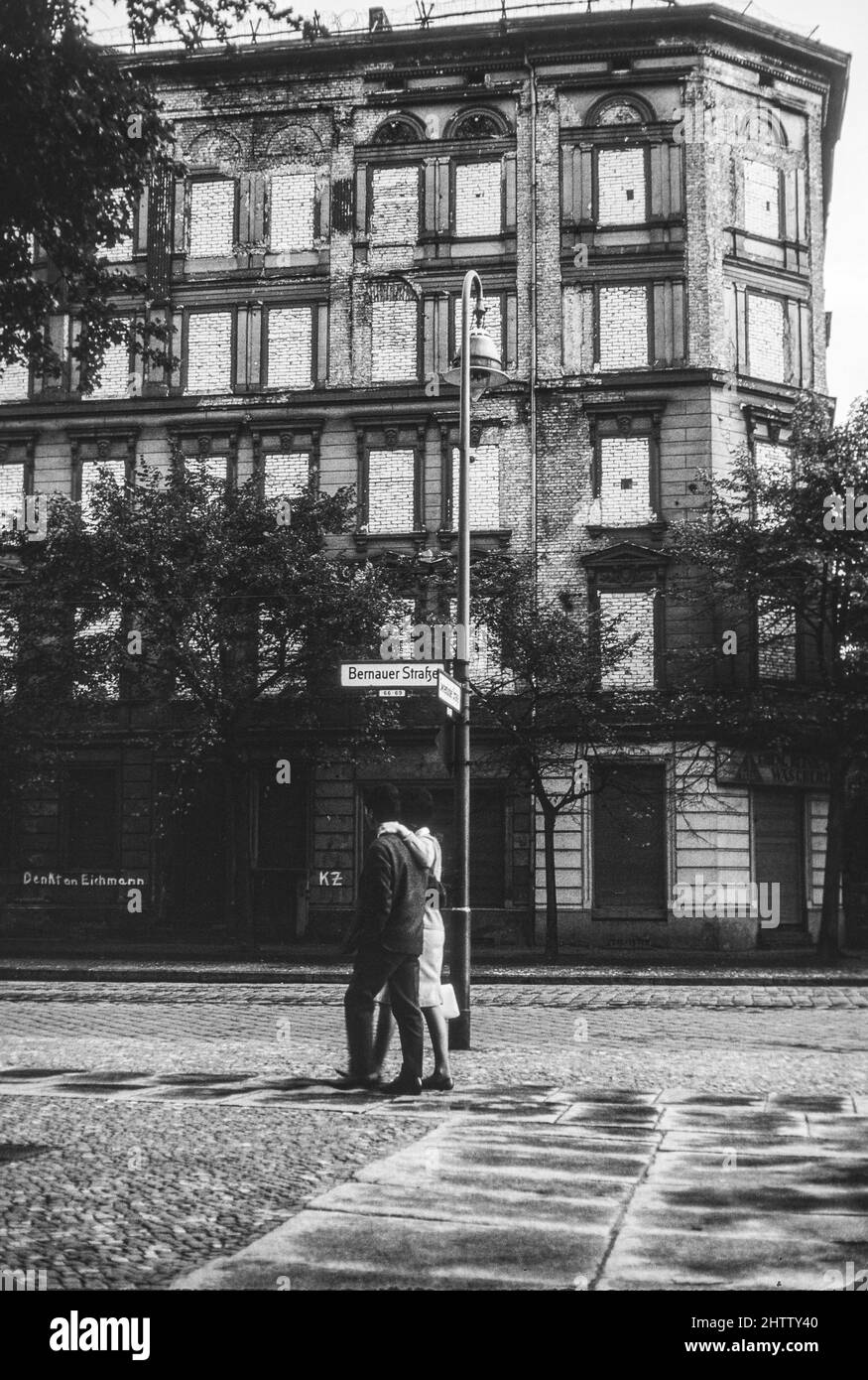 West-Berlin 1962. Ein Paar läuft auf der Bernauer Straße. Beachten Sie, dass Ziegelsteine die Fenster des Wohngebäudes auf der Ost-Berliner Seite der Mauer füllen. Stockfoto