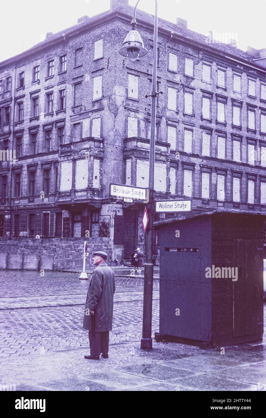 West-Berlin 1962. Mann mittleren Alters an der Ecke Bernauer Straße. Beachten Sie, dass Ziegelsteine die Fenster des Wohngebäudes auf der Ost-Berliner Seite der Mauer füllen. Stockfoto