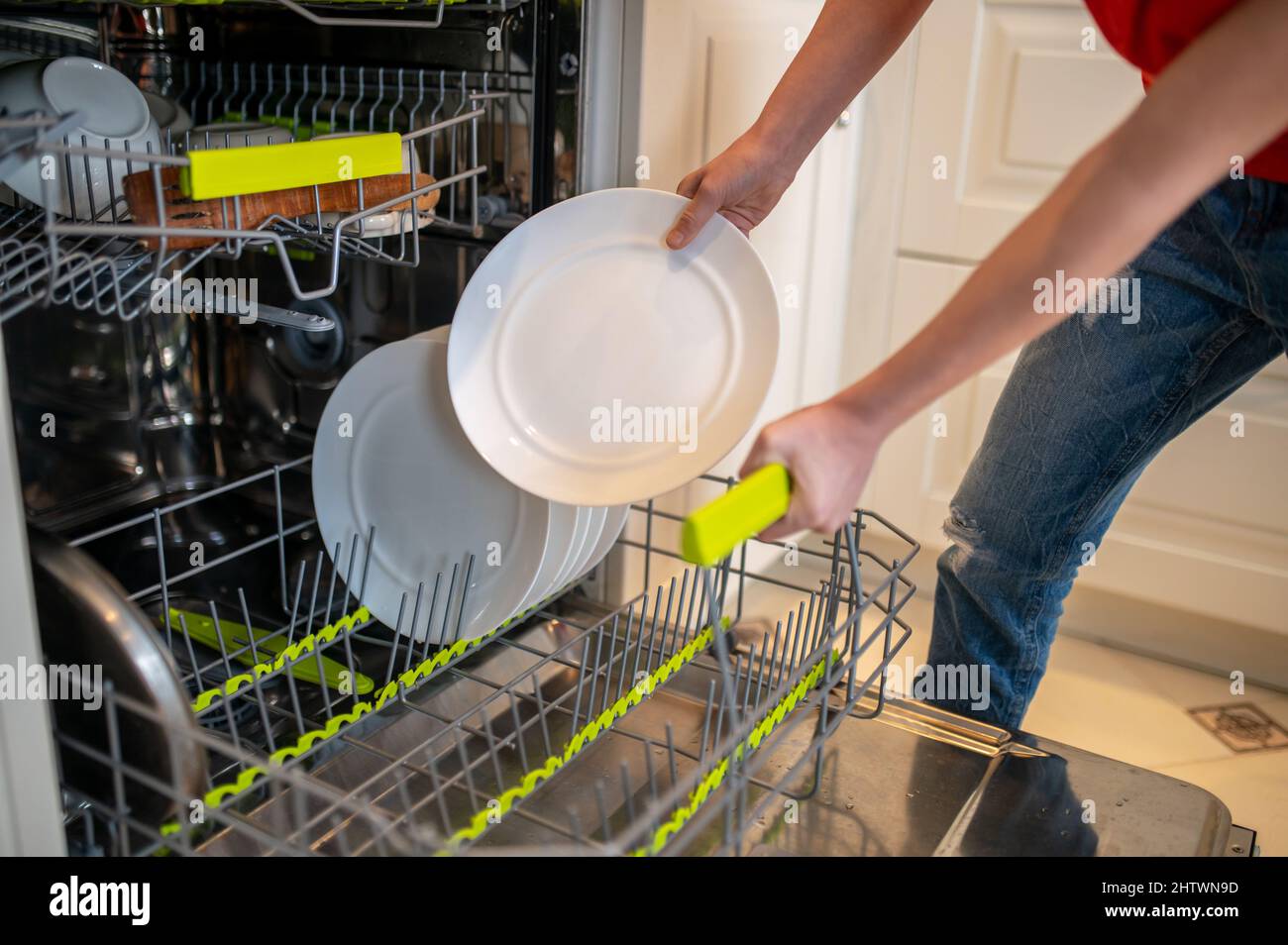 Kind, das ein schmutziges Gericht in eine offene Spülmaschine legt Stockfoto