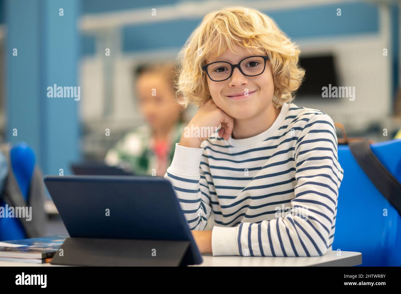 Junge, der die Kamera mit einem Tablet am Schreibtisch anschaut Stockfoto