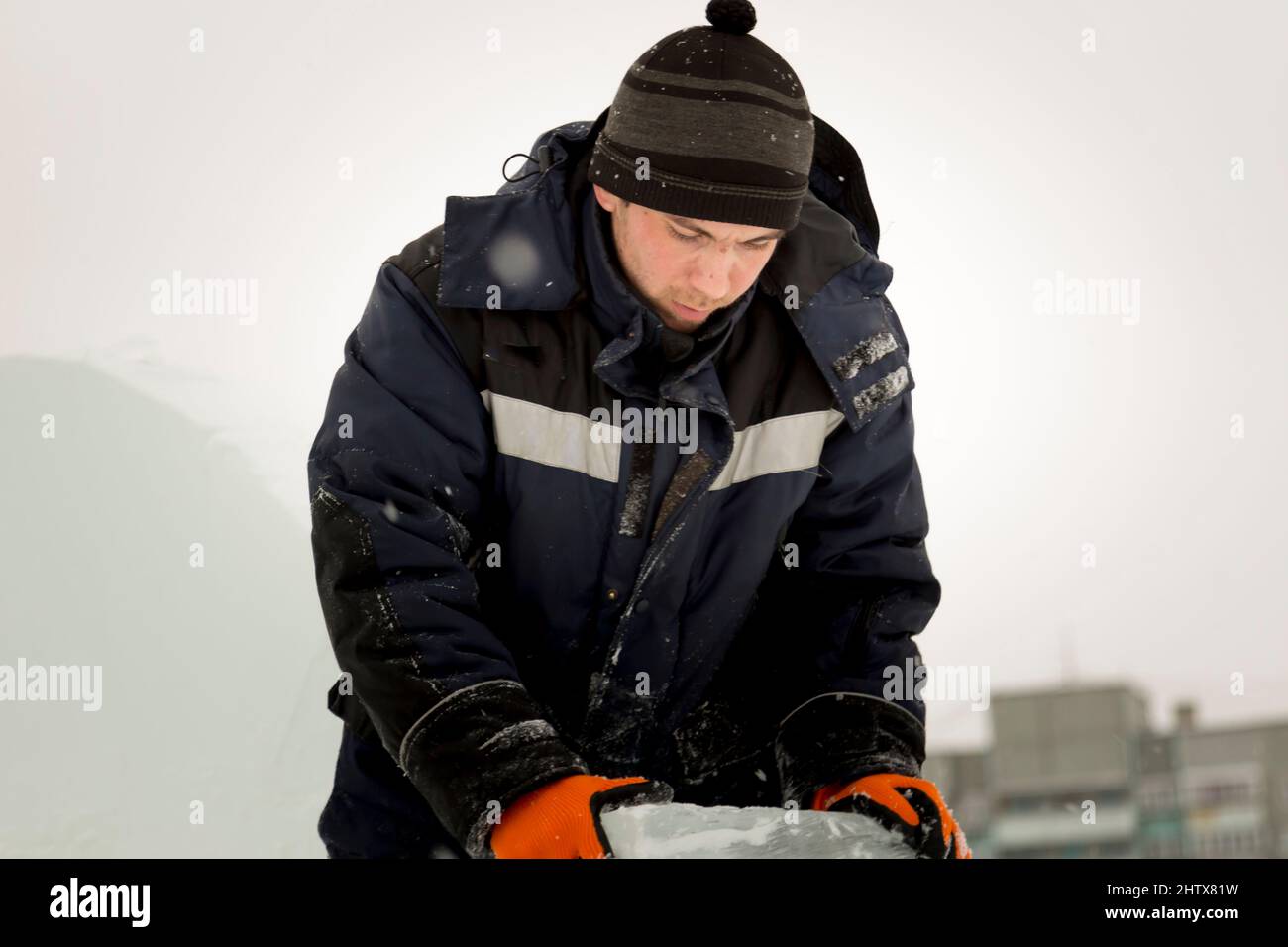 Ein Arbeiter in einer blauen Jacke und einem gestrickten schwarzen Hut bewegt die Eisplatte mit seinen Händen. Stockfoto