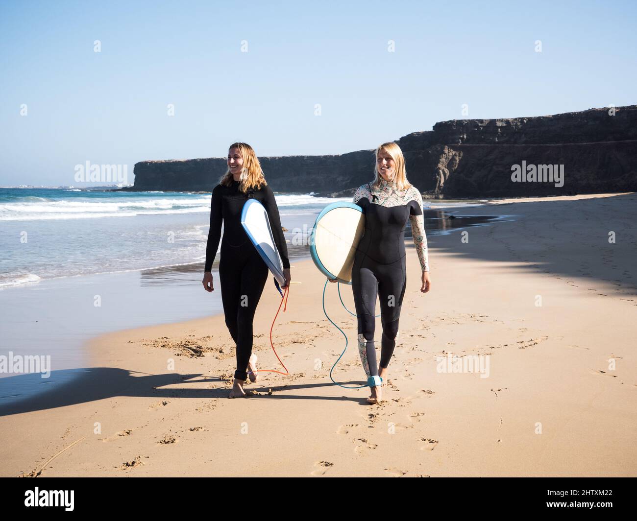 Surferinnen, die am Strand spazieren und auf die Wellen schauen Stockfoto