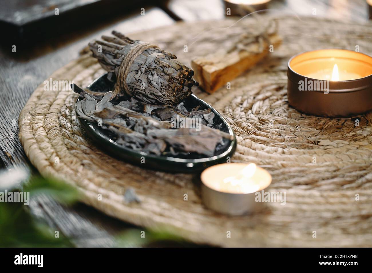 Frau Hände brennen weißen Salbei, vor dem Ritual auf dem Tisch mit Kerzen und grünen Pflanzen. Smoke of smudging behandelt Schmerzen und Stress, klar negativ Stockfoto