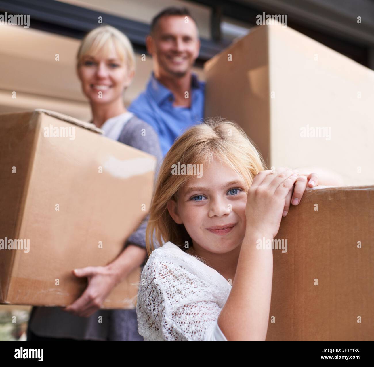 Wir gingen in unser neues Haus. Eine dreiköpfige Familie trägt Kisten in ihr neues Zuhause. Stockfoto