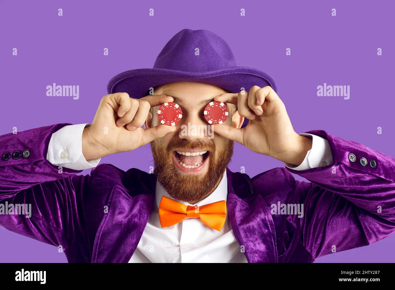 Porträt eines lustigen Mannes in violettem Anzug, der zwei Pokerchips auf den Augen hält und lächelt Stockfoto