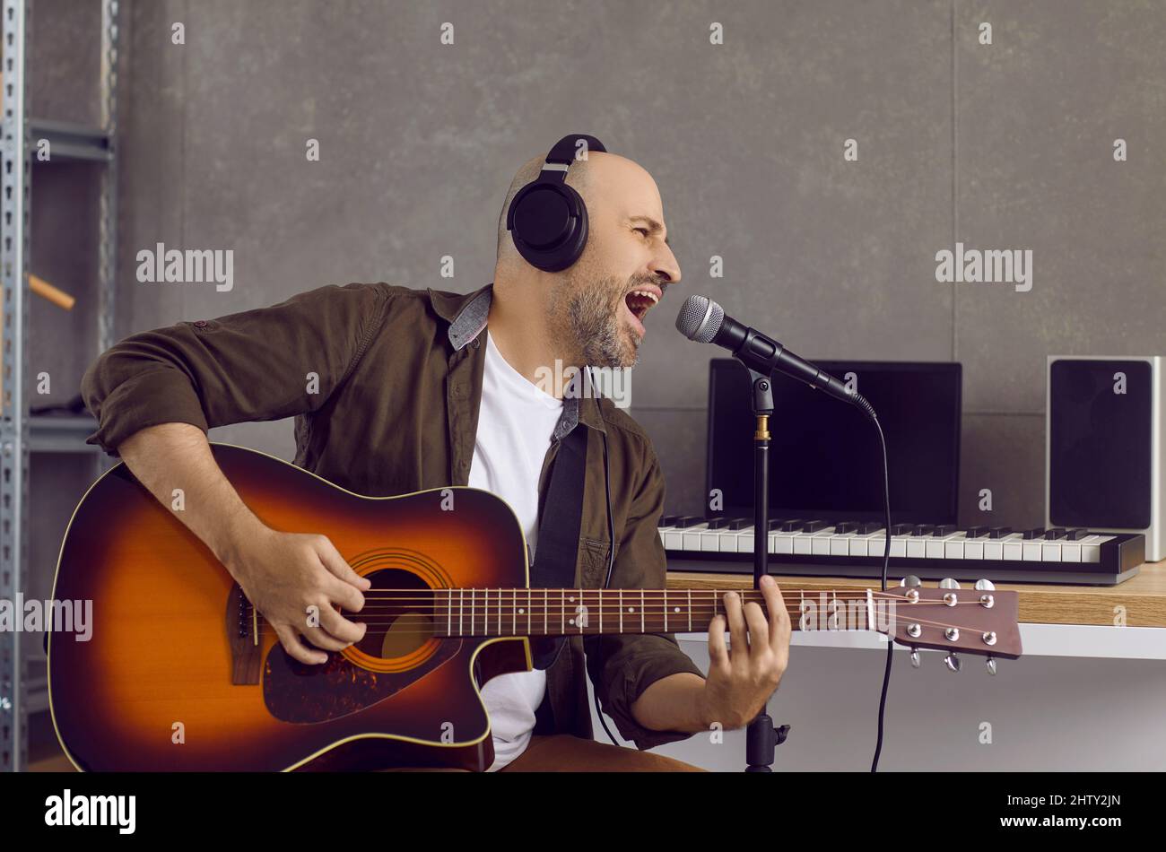 Portrait eines Mannes, der im Studio Musik aufnimmt und ins Mikrofon singt und Gitarre spielt. Stockfoto