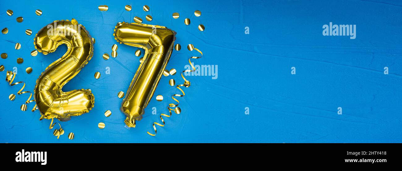 goldene Folienballon Zahl siebenundzwanzig. Geburtstags- oder Jubiläumskarte mit der Aufschrift 27. Blauer Betonhintergrund. Jubiläumsfeier. Bann Stockfoto