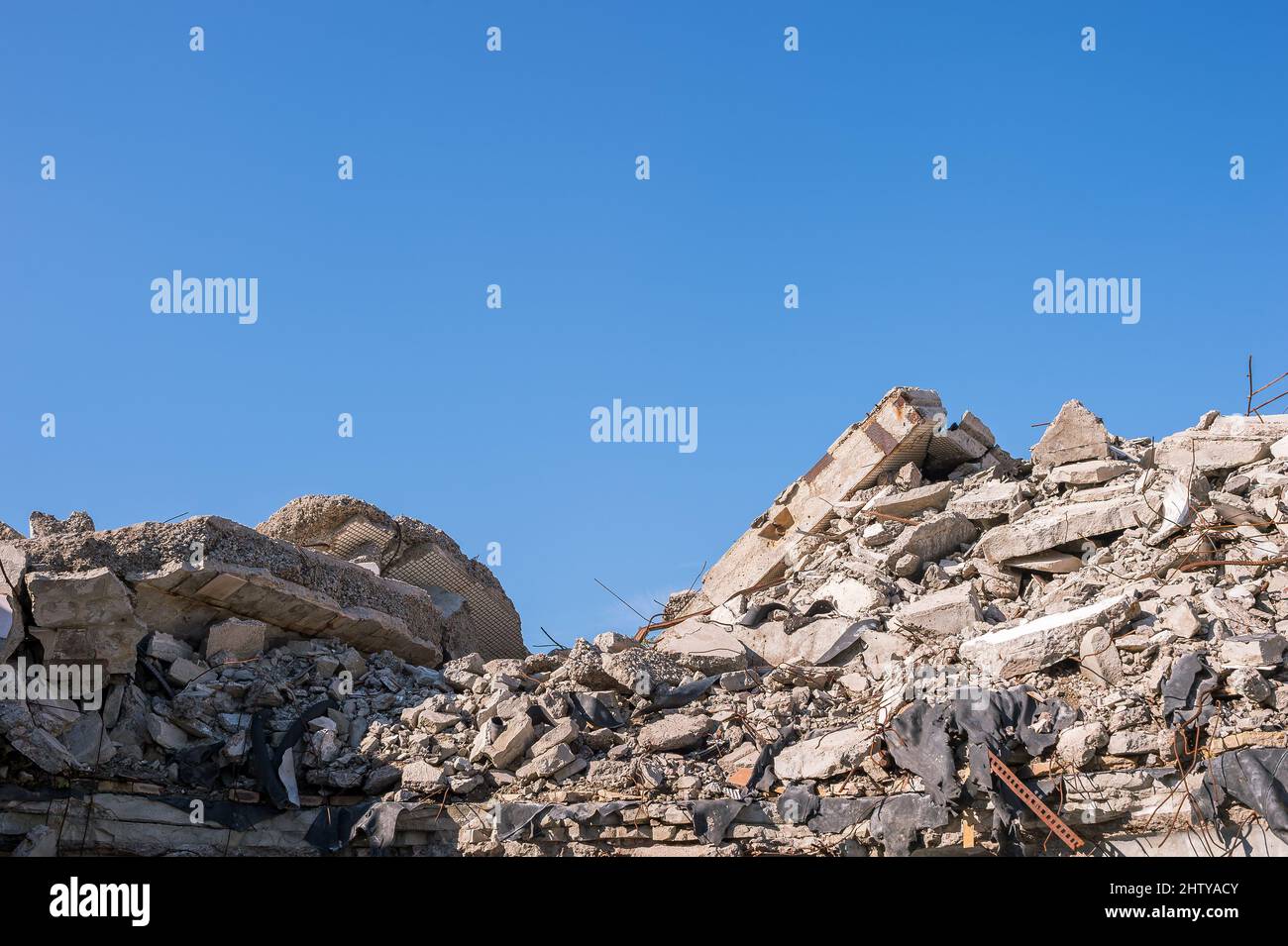 Haufen Bauabfälle in Form von Betonfragmenten aus Platten, Pfählen, Ziegel an einem sonnigen Tag gegen einen blauen, klaren Himmel. Hintergrund. Stockfoto