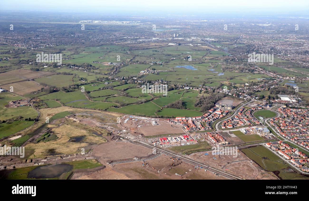 Luftaufnahme eines neuen Wohnbaus auf dem ehemaligen Woodford Aerodrome in der Nähe von Manchester mit dem Flughafen und der Skyline der Stadt in der Ferne Stockfoto