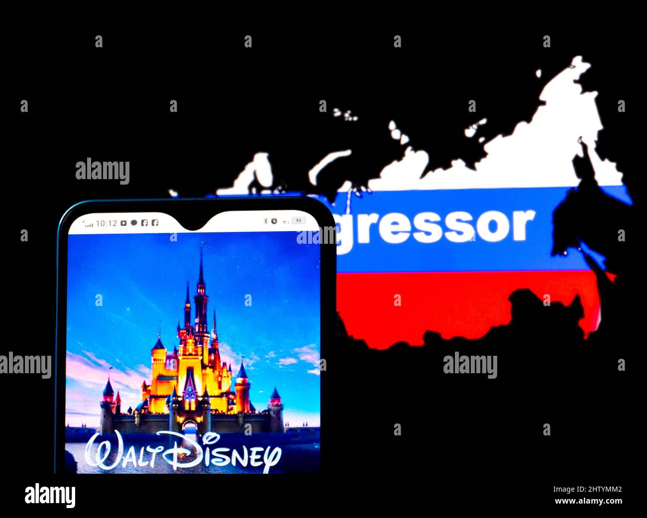 In dieser Fotobilder wird das Walt Disney-Logo auf einem Smartphone-Bildschirm mit einer russischen Flagge in Form einer Landkarte des Landes mit der Aufschrift Aggressor im Hintergrund angezeigt. Walt Disney hat sich den Sanktionen gegen Russland angeschlossen. Stockfoto