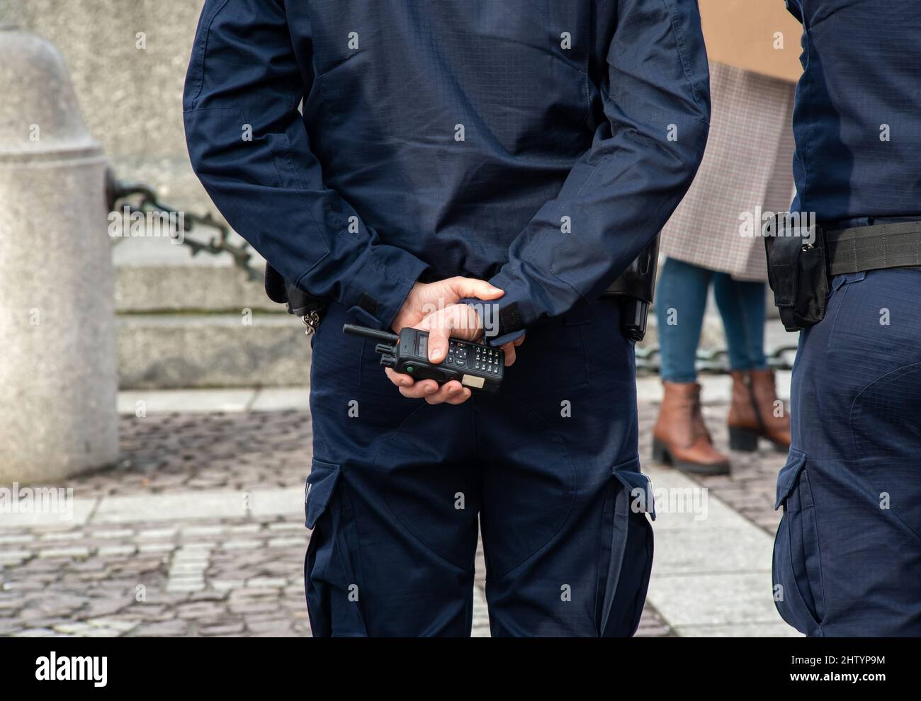 Ein anonymer Polizist in blauer Uniform mit Walkie-Talkie-Radio, Händen in Nahaufnahme, Armen hinter dem Rücken. Kommunikation, Polizeipatrouille-Konzept, unreco Stockfoto