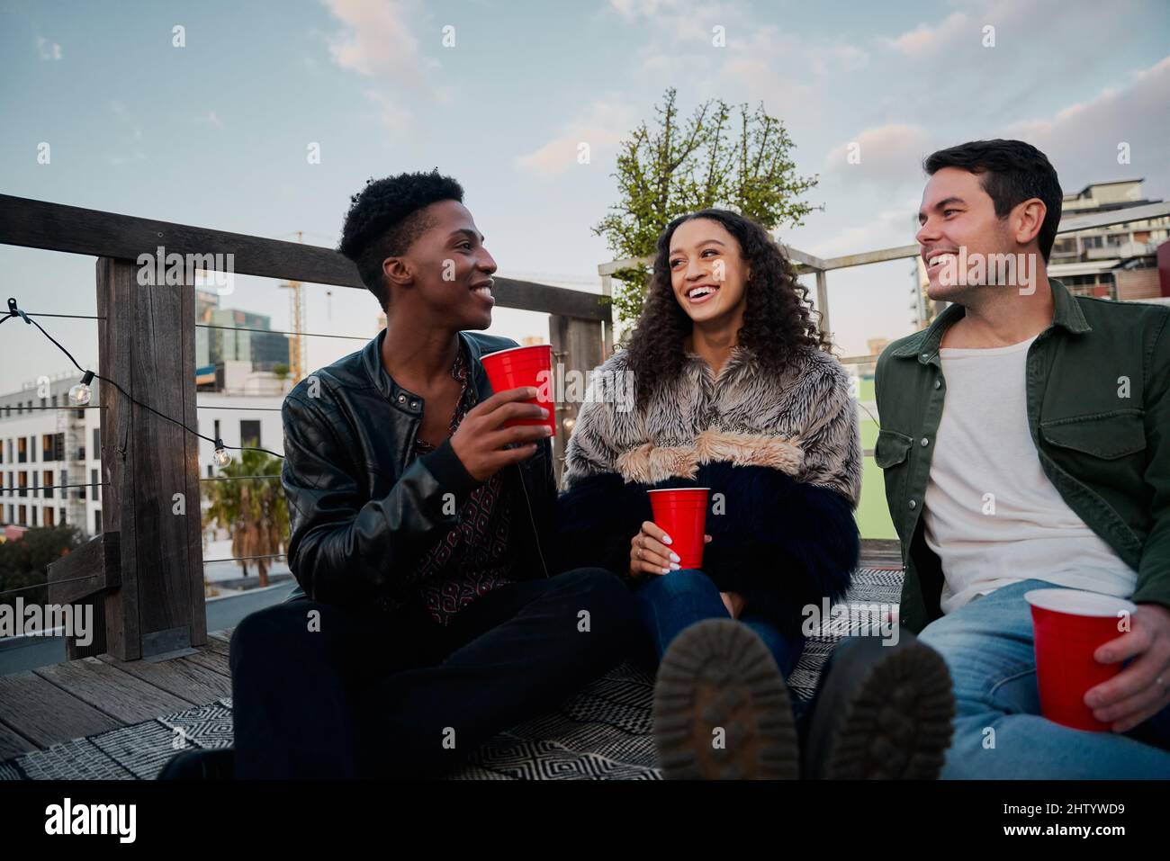 Eine Gruppe multikultureller junger Erwachsener bei einer Dachparty in der Stadt. Gute Zeiten, lächelnd aufeinander. Stockfoto