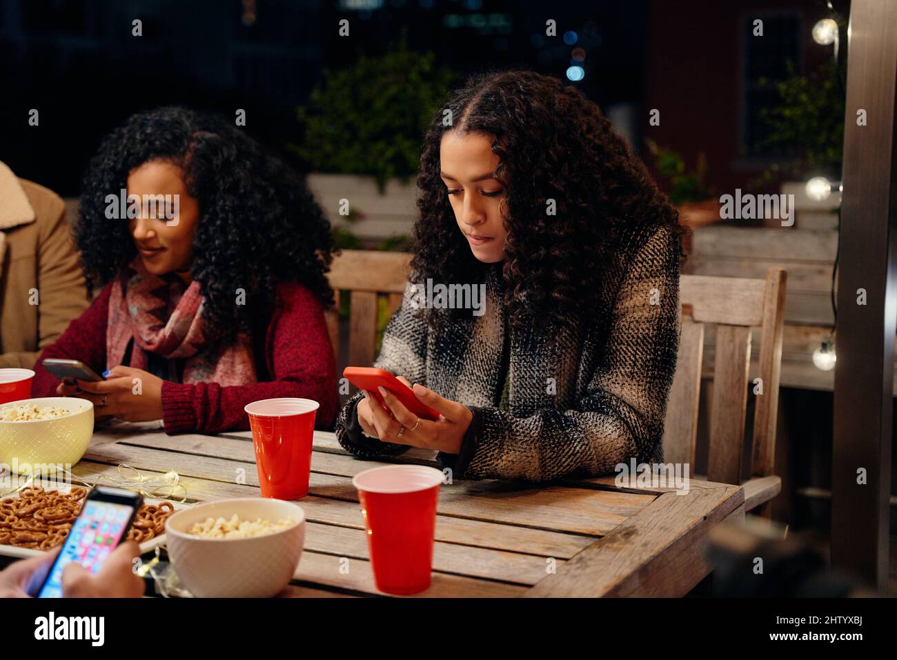 Zwei Frauen mit birazialem jungen Erwachsenen, die auf einer Party sitzen und eine SMS an ihr Telefon senden. Antisozial, mit Technologie auf der Dachparty Stockfoto