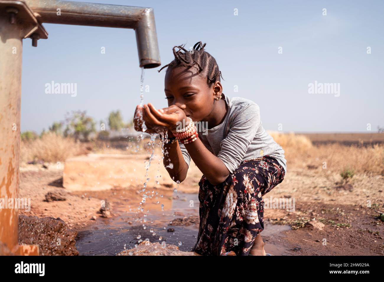 Ein junges schwarzes Mädchen trinkt gierig frisches Wasser aus einem Rohr irgendwo in einem afrikanischen Trockenland; Konzept der globalen Erwärmung Stockfoto