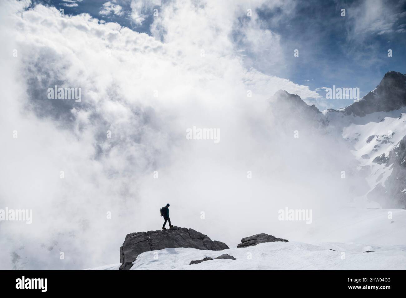 Person, die auf dem Rand eines Felsens inmitten einer verschneiten Landschaft unter den Wolken steht Stockfoto