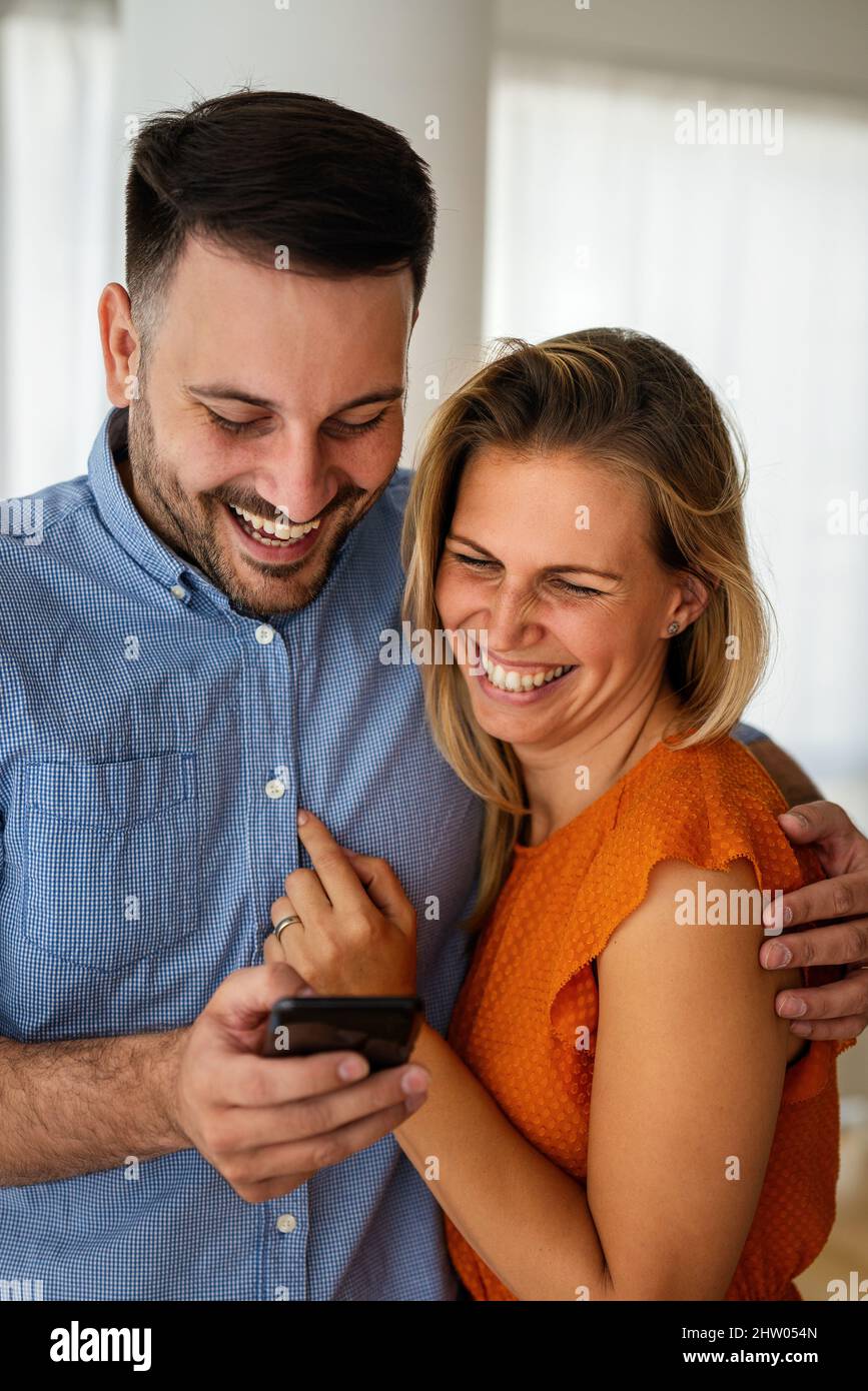 Lächelndes Paar, das sich mit einem Smartphone umarmt. Menschen, die soziale Medien auf dem Mobiltelefon teilen. Stockfoto