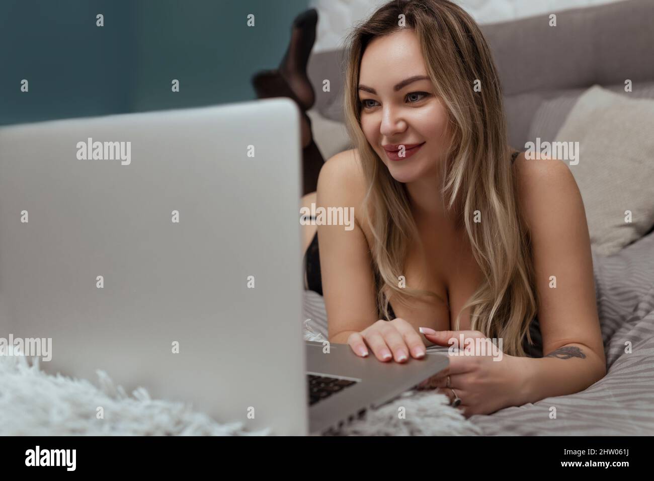 Sexy Frau in schwarzen Dessous liegt auf dem Bett und nutzt einen Laptop. Sex-Modell Konzept auf Webcam und Dating-Website Stockfoto