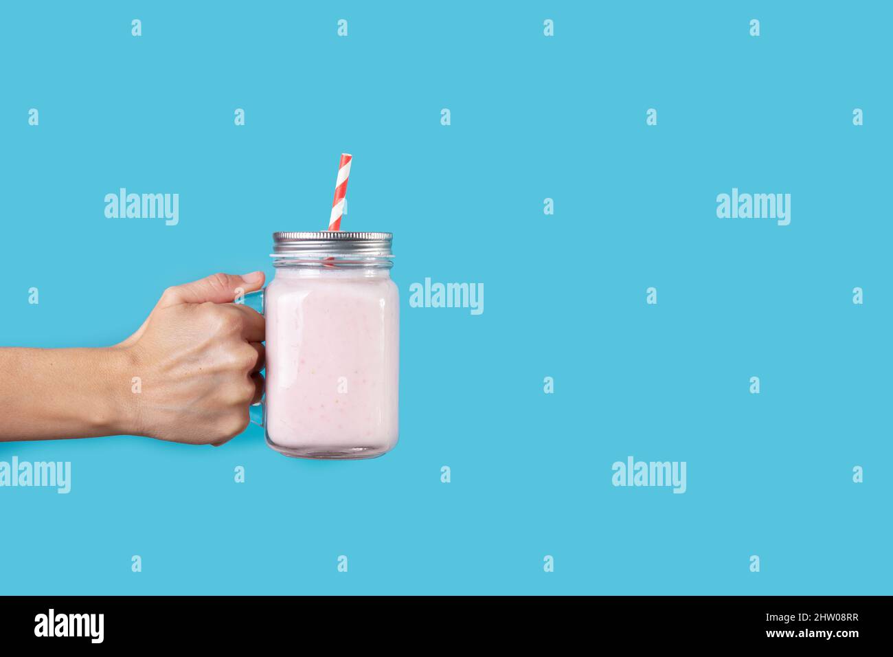 Hand mit Erdbeer-Smoothie-Glas auf blauem Hintergrund Stockfoto