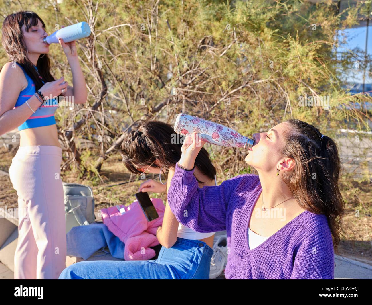 Drei junge Frauen trinken nach dem Skaten in einem Park Wasser Stockfoto