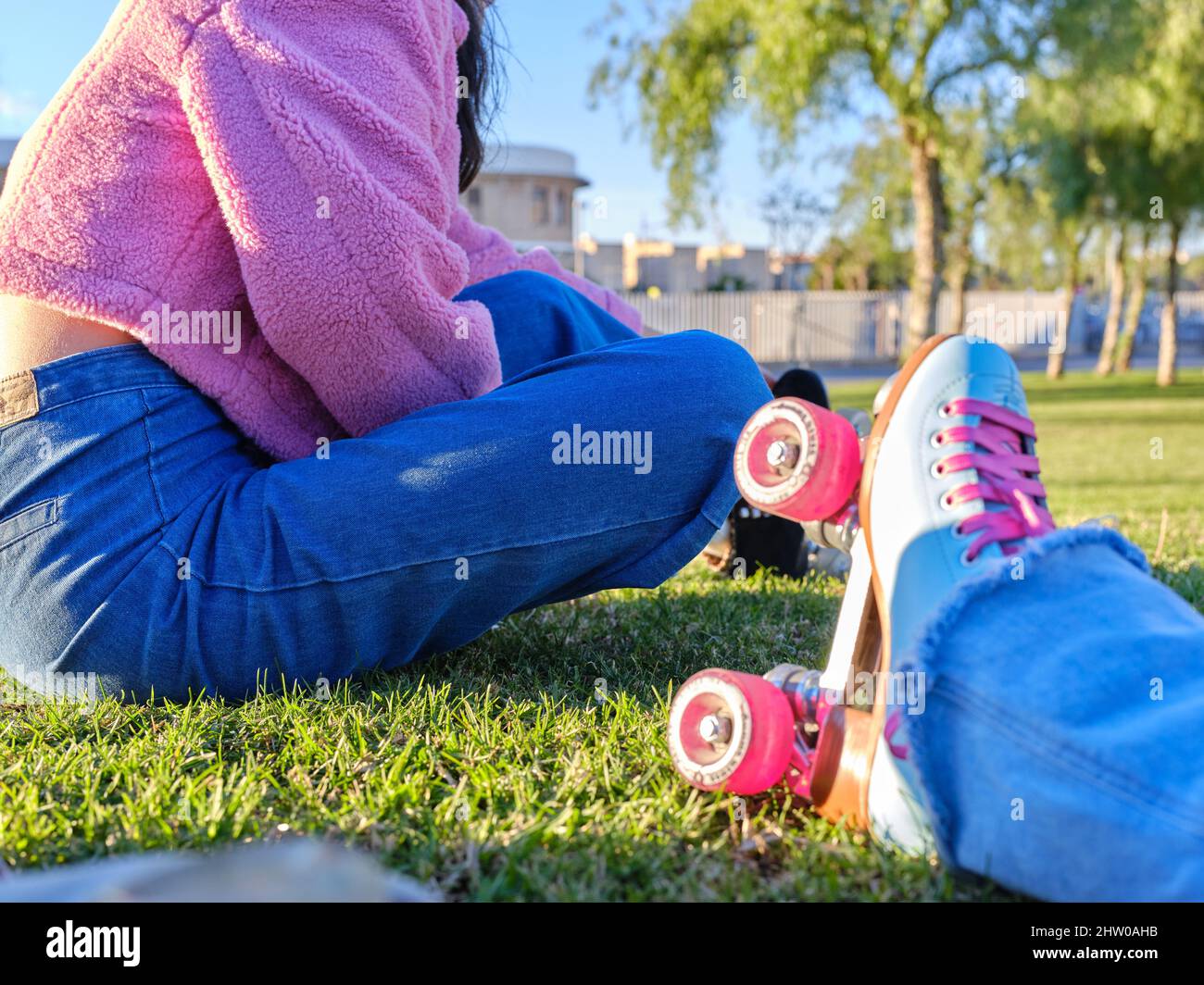 Bein einer Frau mit klassischem Skate im Vintage-Stil neben einem Mädchen, das in einem Park sitzt Stockfoto