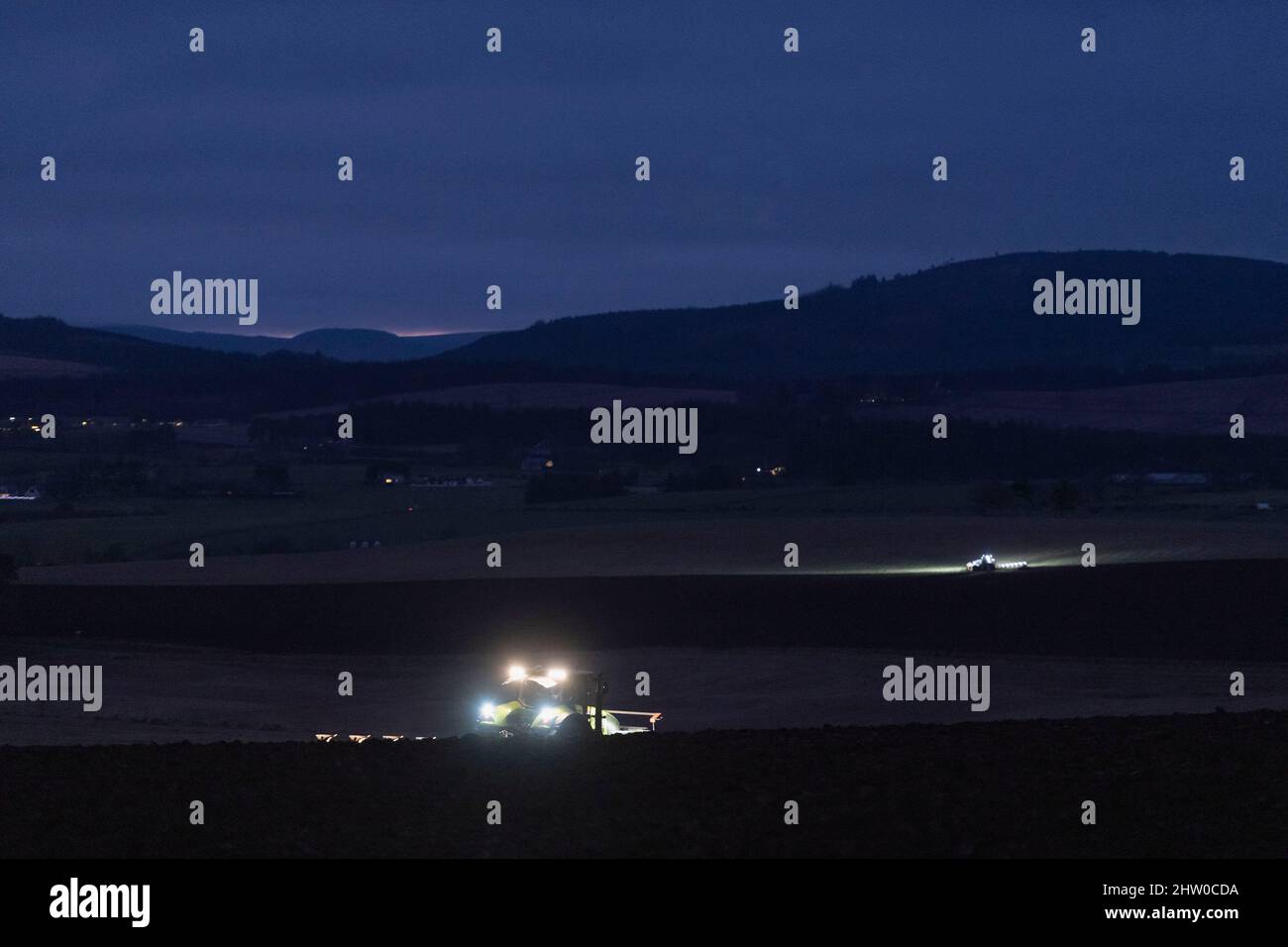 Ein Blick über Aberdeenshire Farmland an einem Winterabend mit zwei Traktoren, die nach Einbruch der Dunkelheit noch pflügen Stockfoto