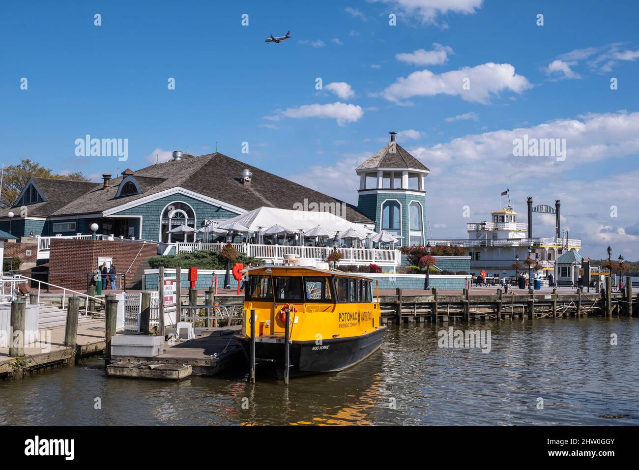 Alexandria, Virginia Waterfront. Das Chart House Restaurant, Potomac Water Taxi und das Cherry Blossom Riverboat im Hintergrund rechts. Flugzeuganflug Stockfoto