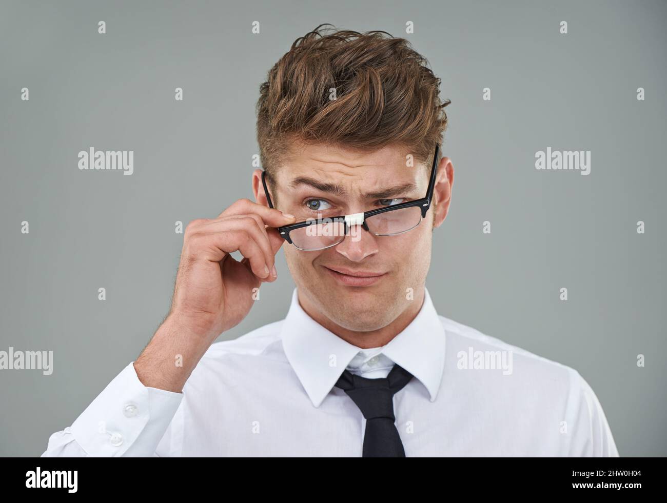 Hes ein wenig skeptisch Ein junger Mann, der skeptisch über seine Brille schaut. Stockfoto