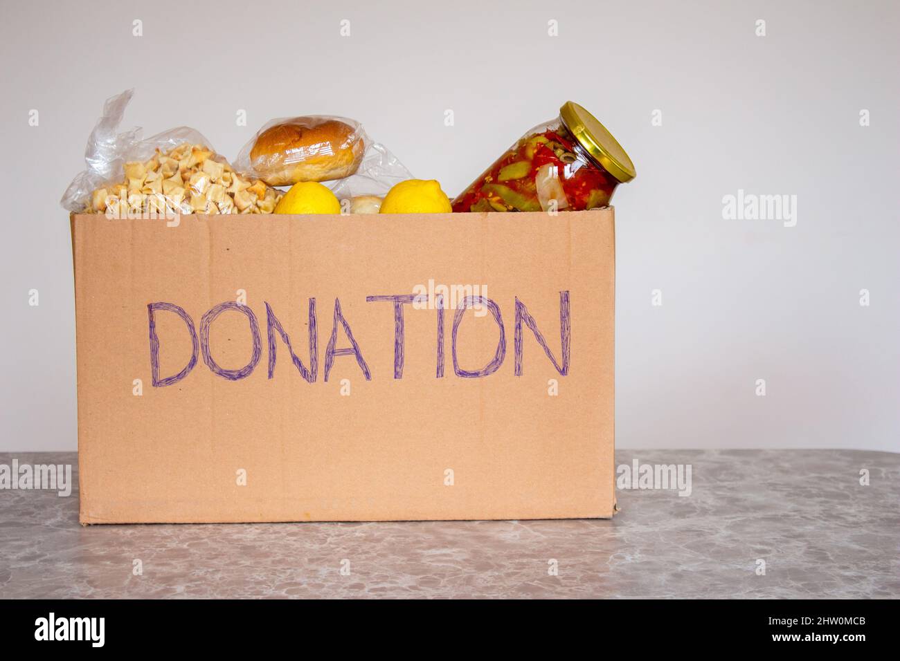 Spendenbox für Lebensmittel auf Marmortisch. Nahrungsmittelhilfe für bedürftige Menschen. Stockfoto