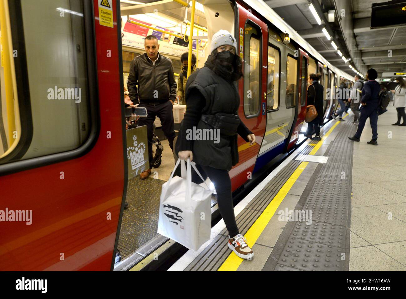 London, England, Großbritannien. U-Bahnstation Westminster - Menschen, die aus einem Zug steigen, tragen Anti-COVID-Masken, Februar 2022 Stockfoto