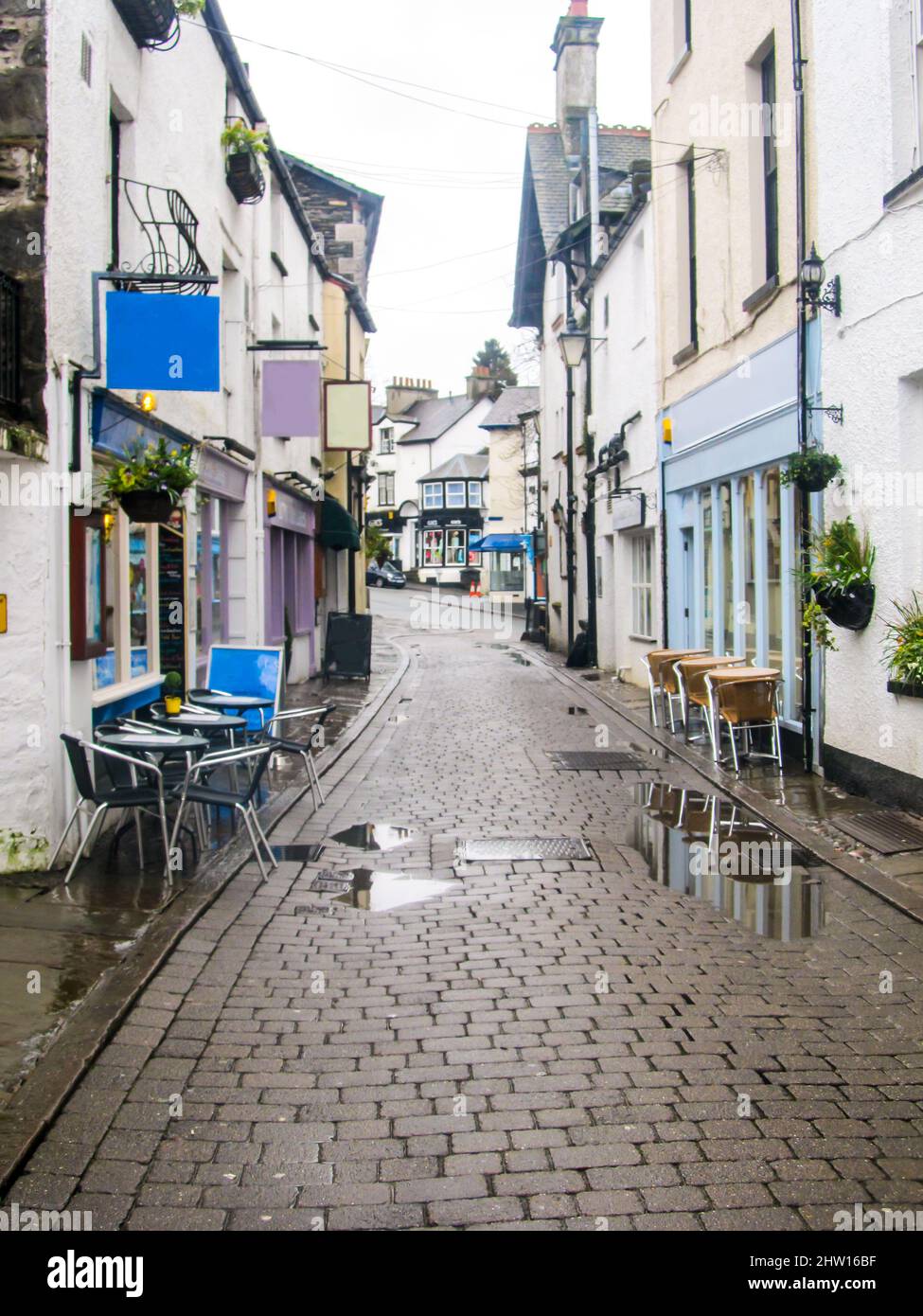 Eine kleine, verlassene gepflasterte Straße mit Cafés, die sich nach einer Regendusche durch die kleine Stadt Bowness-on-Windermere, Großbritannien, schlängelt Stockfoto