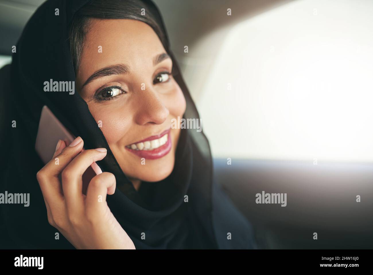 Führungskräfte verlangen Führungsreisen. Aufnahme einer jungen muslimischen Geschäftsfrau, die ihr Telefon benutzte, während sie in einem Auto unterwegs war. Stockfoto