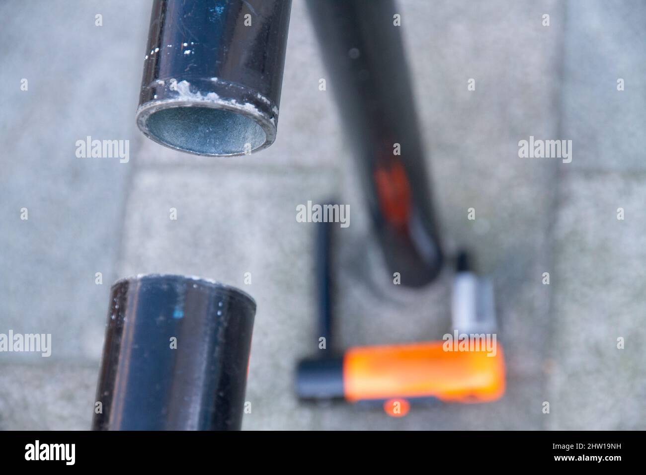 Nahaufnahme eines Fahrradstandrahmens, der durchgeschnitten wurde, um Diebstahl zu ermöglichen. Zeigt eine gebrochene D-Sperre, die auf dem Boden unscharf ist Stockfoto