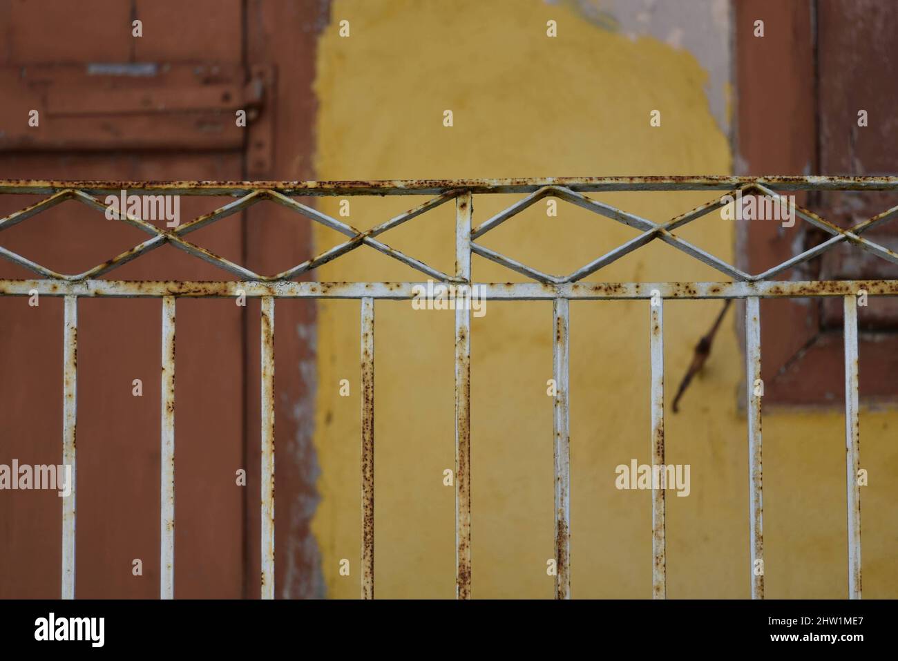 Alte ländliche Hausfassade mit einer ockerfarbenen Stuckwand, braunen Fensterläden aus Holz und einem rostig verwitterten schmiedeeisernen Balkongeländer in Nafplio, Griechenland. Stockfoto